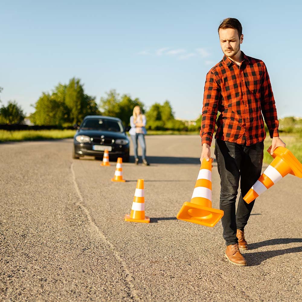 Male instructor puts traffic cones on road, driving school. Man teaching lady to drive vehicle. Driver's license education