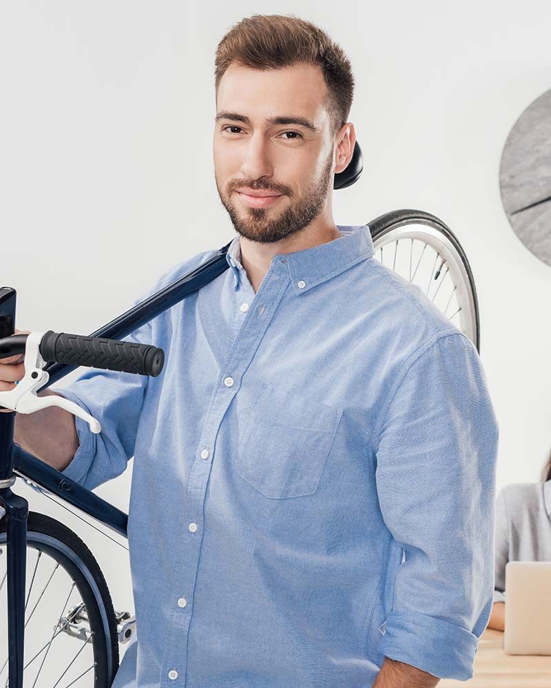 portrait of businessman holding bicycle while colleagues working on laptop in office