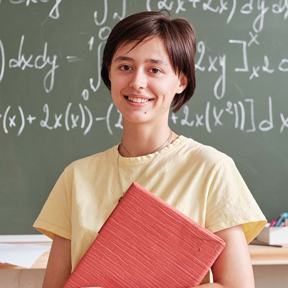 Portrait of teacher with books smiling at camera standing against the blackboard and teaching at university