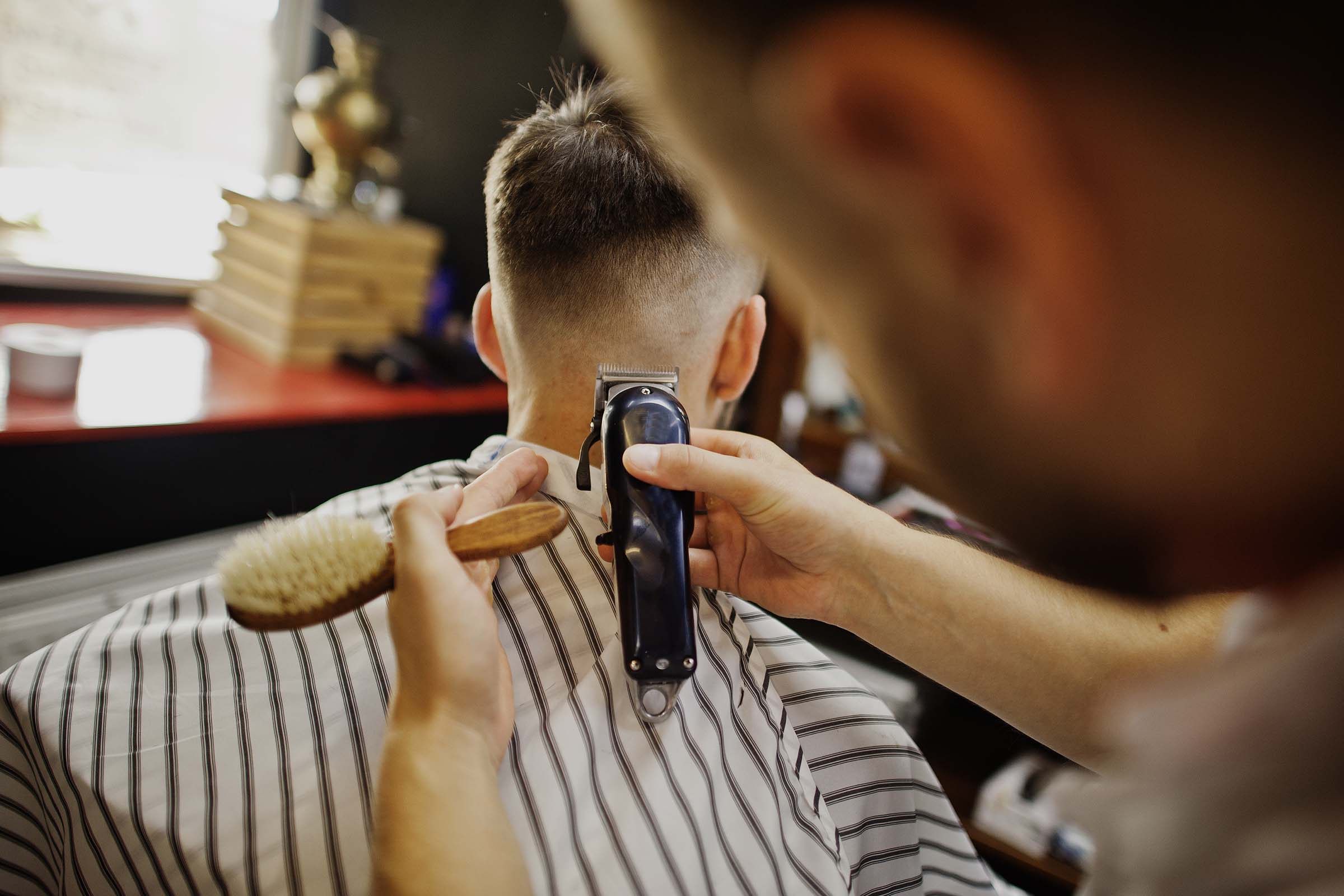 Young bearded man getting haircut by hairdresser while sitting in chair at barbershop. Barber soul.