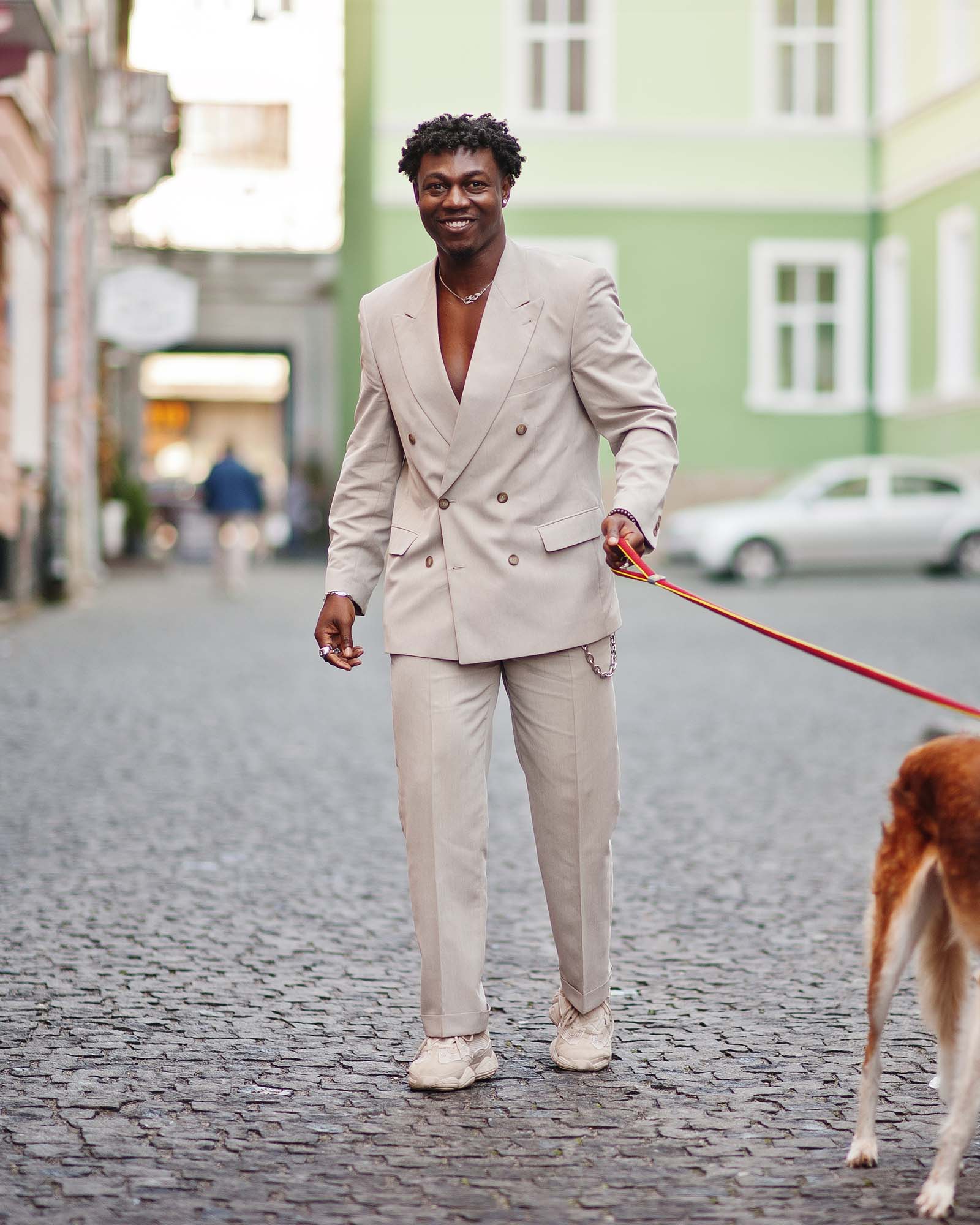 Stylish afro man in beige old school suit with Russian Borzoi dog. Fashionable young African male in casual jacket on bare torso.